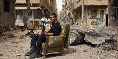 Un miembro del Ej&eacute;rcito Libre Sirio sujeta un arma, sentado en medio de una calle de Deir el Zor, el jueves.