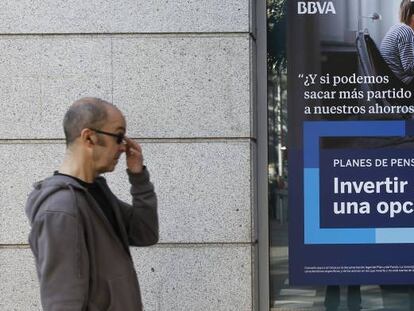 Una persona pasa delante de una oficina de BBVA donde se promocionan planes de pensiones.