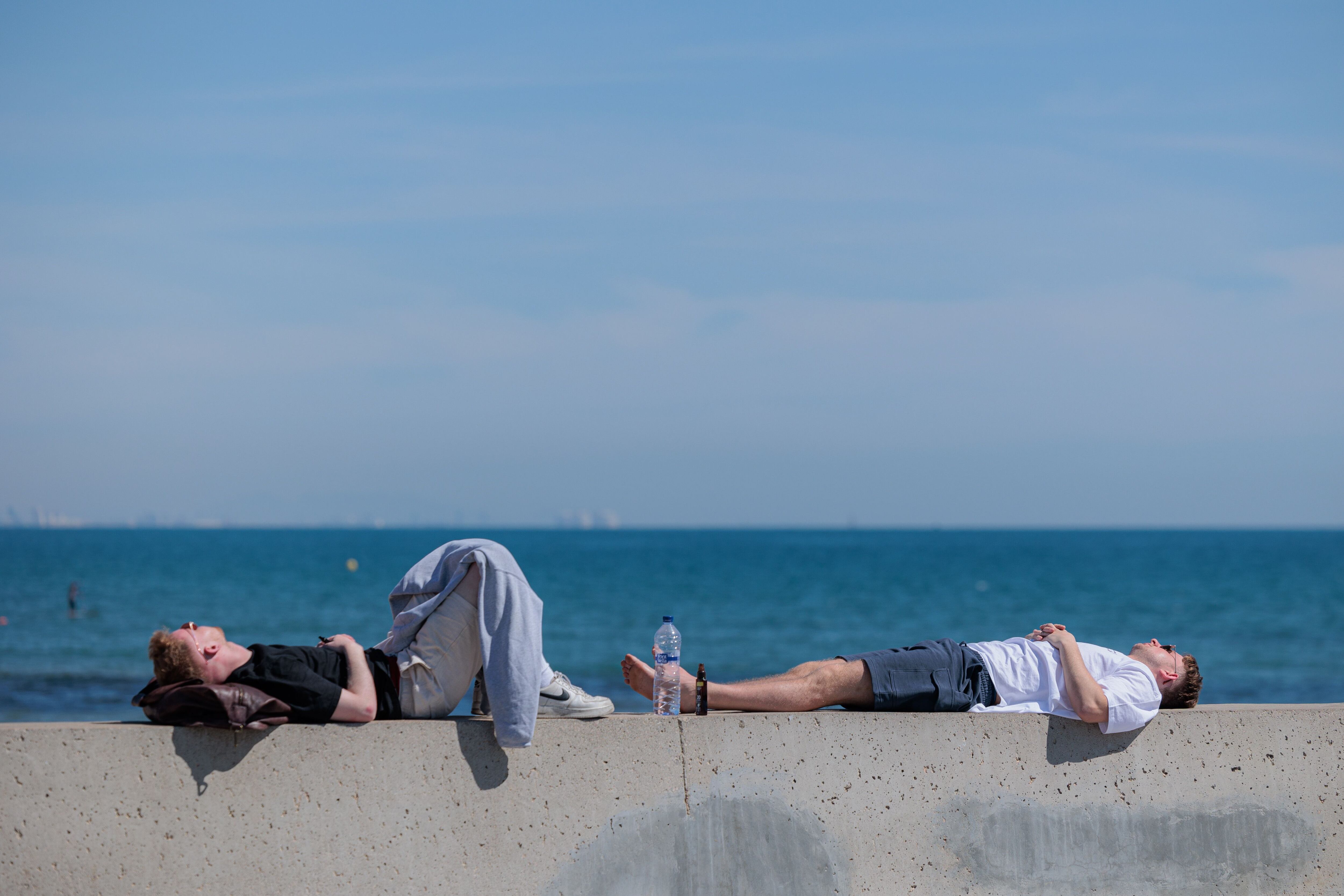 Dos personas descansan al sol en la playa de la Malvarrosa, en Valencia