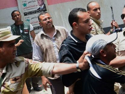 Un policía armado detiene a un hombre por tirar balas de goma en las afueras de un colegio electoral en la ciudad de Mansura.