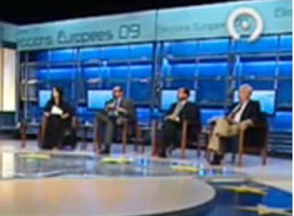 Andrés Perelló, eurodiputado socialista, participa en un debate electoral y critica los informativos de Canal 9. La presentadora le corta y alega que debe hablar de economía. Perrelló recuerda que tiene tres minutos y sigue adelante.