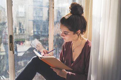 Una adolescente escribe junto a su ventana.