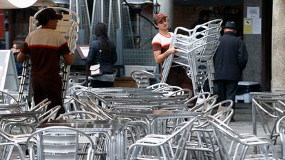 Varios trabajadores preparan las mesas de una terraza en un bar.