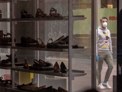 Un hombre protegido con mascarilla visto a través del escaparate de una tienda de zapatos cerrada en Sevilla.