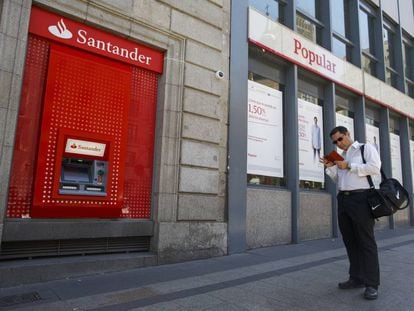 Un hombre mira su m&oacute;vil ante dos oficinas de Santander y Popular.