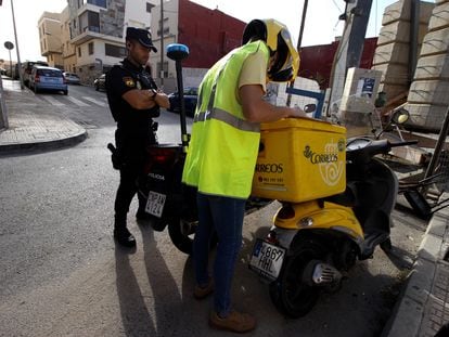 Un agente de la Policía Nacional escolta a un cartero que reparte la documentación para votar por correo en el barrio de La Libertad, en Melilla, en la tarde de este jueves.