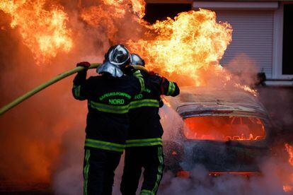Dos bomberos apagan las llamas de un coche incendiado durante las protestas en Lille, al norte de Francia, este jueves. 