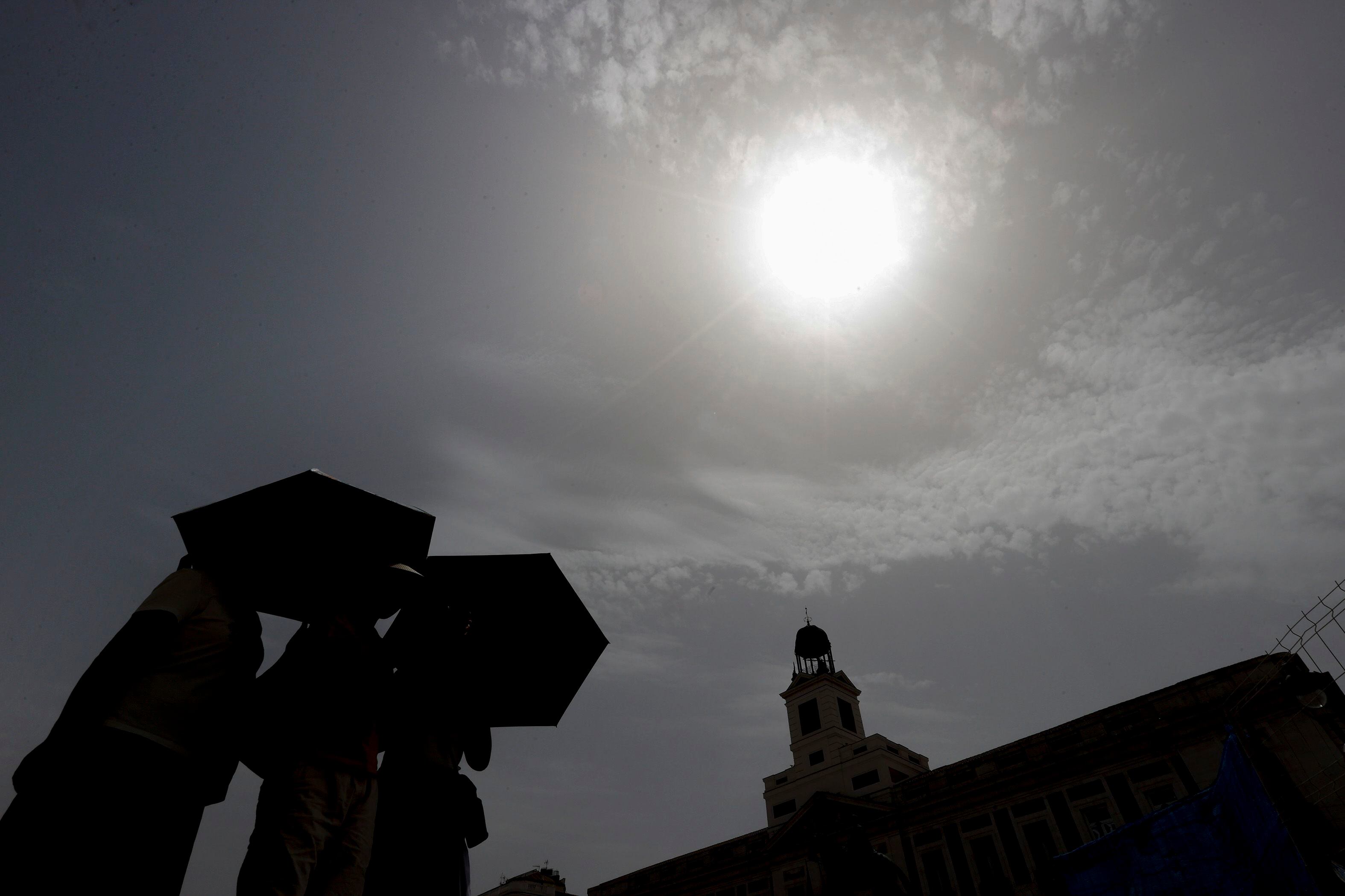 Varios viandantes se protegen del sol mientras cruzan la Puerta del Sol de Madrid, este miércoles.