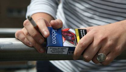 Un joven fumando con una cajetilla de tabaco en la mano