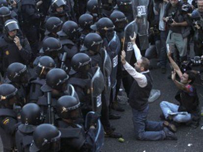 Dos manifestantes con los brazos levantados frente a dos filas de agentes antidisturbios en el 25-S.