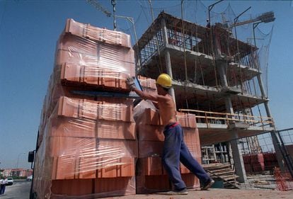 Un obrero con el torso desnudo y su casco reglamentario manipula una carga de ladrillos para transportarlos con una grúa durante la construcción de un edificio de viviendas en Madrid. La imagen es de julio de 1999.