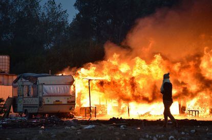 Una mujer pasa delante de una caravana incendiada en la desmantelada 'Jungla' de Calais.