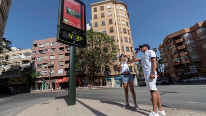Dos jóvenes beben agua junto a un termómetro que marca 43 grados, el martes en laplaza del Royo de Murcia.