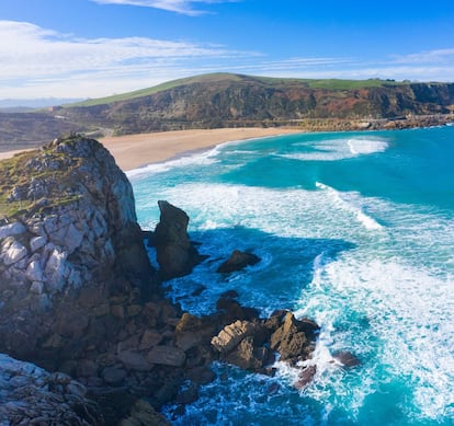 Ejemplo de playa de arena blanca, tan asilvestrada como peligrosa para el baño. Cuando el mar castiga Liencres, Usgo atrae a los surfistas de la comarca, entre ellos a los del Special Surf School (<a href="https://specialsurf.com/" target="_blank">specialsurf.com</a>), del tres veces campeón de Europa Dani García. Las caribeñas franjas azul claro en el agua son producto de la solución salina vertida por la empresa Solvay. <BR></BR>En la imagen, vista del arenal de Usgo, una playa encajada entre acantilados en la localidad cántabra de Miengo.
