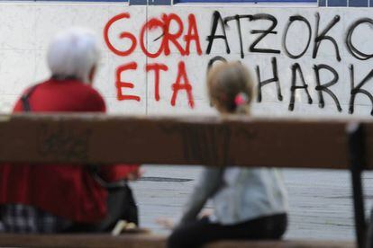 Dos personas sentadas ante una de las pintadas en favor de ETA, en Vitoria.