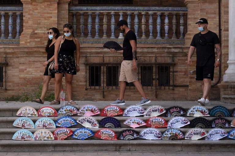 Un grupo de turistas pasan por un puesto ambulante de abanicos en la Plaza de España en Sevilla.