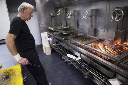 Bittor Arginzoniz prepara una chuleta a la brasa en su cocina, donde hay parrillas de acero y titanio, que sube y baja con poleas para acercar o alejar los alimentos del fuego.