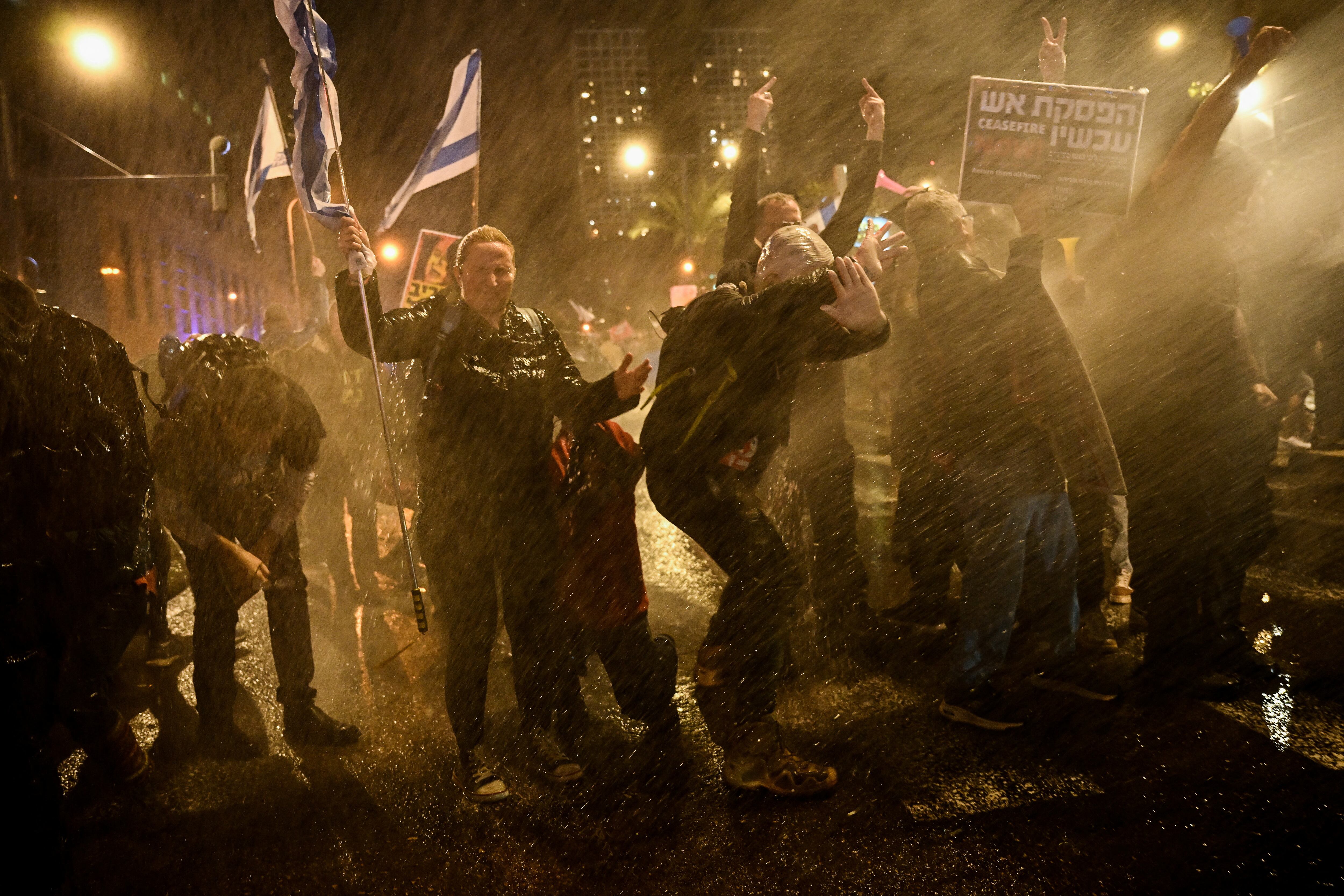 SENSITIVE MATERIAL. THIS IMAGE MAY OFFEND OR DISTURB People hold Israeli flags and gesture as police use water cannons to disperse demonstrators during a protest against Israeli Prime Minister Benjamin Netanyahu's government, amid the ongoing conflict between Israel and the Palestinian Islamist group Hamas from Gaza, in Tel Aviv, Israel, February 24, 2024. REUTERS/Dylan Martinez