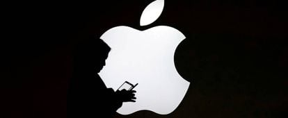 Una persona consulta un móvil delante de un logotipo de Apple, en Shangai.