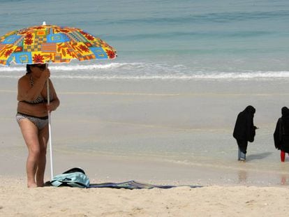 Una turista coloca una sombrilla mientras dos mujeres se mojan los pies en una playa de Dub&aacute;i.