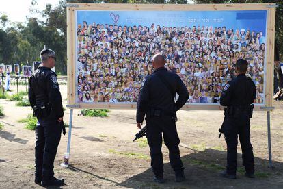 Several police officers observe a panel with photos of the victims at the Nova festival before accompanying the hostages' relatives as they leave the march.