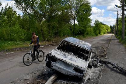Un hombre en bicicleta pasa junto a un coche destruido por un bombardeo en una calle a las afueras de Niu-York, en Donetsk, este lunes.