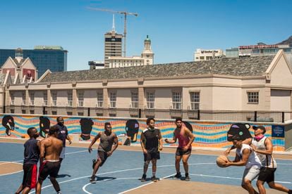Unos chicos juegan un partido de baloncesto en el área Victoria & Albert Waterfront de Ciudad del Cabo, Sudáfrica, en diciembre de 2020, al comienzo de la segunda ola de covid-19 en este país. Pincha en la imagen para ver la fotogalería completa.