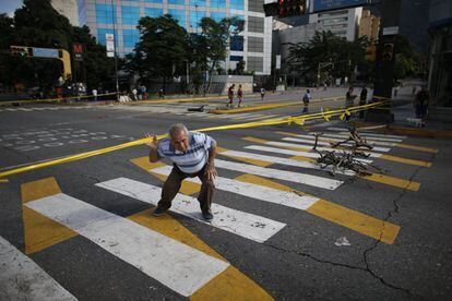 Un peatón atraviesa una cinta colocada por protestantes opositores al gobierno de Maduro para cerrar el trafico en una intersección en Caracas.