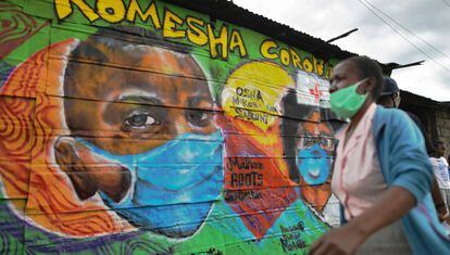 Una mujer con mascarilla pasa por delante de una pintura mural en la que se lee 'Komesha Corona' ("Acabemos con el corona", en suajili) en el barrio de Mathare de la capital de Kenia, 29 de abril de 2020.