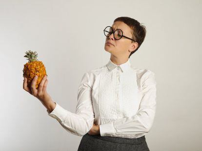 Una mujer mira el ananás que tiene en la mano.