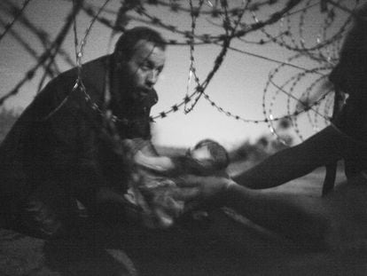 Esta imagen del fotógrafo australiano Warren Richardson ha sido la ganadora de la 59 edición de la fotografía del año World Press Photo, la máxima distinción del fotoperiodismo mundial. La fotografía, en blanco y negro, muestra un hombre pasando a un bebe a través de la valla de alambre de espino en Roeszke, en la frontera entre Serbia y Hungría, el 28 de agosto de 2015. "Yo estaba en el lado serbio, donde casi no había policía, apenas un coche y no estaban haciendo nada. Los refugiados podían tener problemas en el lado húngaro si se encontraban con los guardias fronterizos", ha explicado Richardson. La foto, continúa, está tomada de noche y sin flash, porque si la hubiera hecho con flash la policía habría venido. Richardson mandó la imagen a varias agencias de noticias, pero ese verano ninguna quiso comprársela. "La subí a la red social Facebook y unas 29 personas le dieron al botón "me gusta", eso es todo", ha concluido, mientras se encogía de hombros.