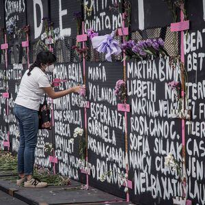 Una mujer pinta una cruz en la valla instalada en el Palacio Nacional en Ciudad de México, el día de hoy.