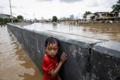 Un niño se protege tras un muro en una carretera inundada de Yakarta (Indonesia). 