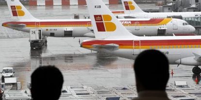 Dos pasajeros observan varios aviones de la compañia Iberia en el aeropuerto de Barajas.