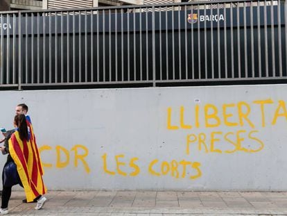 Dos manifestantes independentistas caminan este miércoles por delante del Camp Nou, en Barcelona,ante una pintada que reza "libertad presos cdr Les Corts".