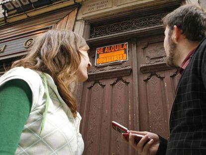 Una pareja apunta en el móvil el número de teléfono de un piso en alquiler.