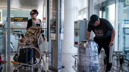 Un embalador se afana a proteger con plástico una maleta, este jueves en el aeropuerto de El Prat.