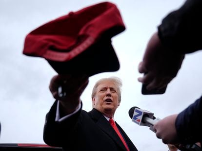 El expresidente Donald Trump entrega una gorra a un seguidor mientras habla los medios durante la campaña en New Hampshire, el 23 de enero de 2024.