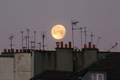 La Luna es vista tras chimeneas y antenas de televisión, en París (Francia).
