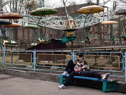 Una pareja mira sus teléfonos junto a una antigua atracción en el Parque de Cultura y Recreación Tarasa Shevchenka, en Berdichev, a finales de marzo.