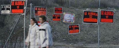 Una pareja pasea ante una valla con carteles de pisos en venta y en alquiler en Madrid.