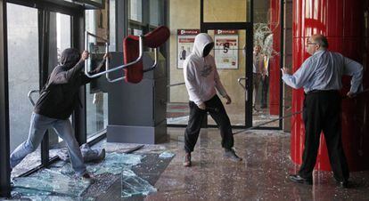 Un empleado de una sucursal bancaria increpa a dos manifestantes que han roto cristales en una entidad bancaria situada en el Paseo de Gracia, junto al edificio de la Bolsa de Barcelona.