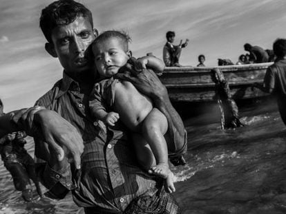 Un refugiado rohingya lleva en sus brazos a un bebé después de llegar en barco a Bangladesh después de huir de su pueblo en Myanmar, el 1 de octubre de 2017 en Cox's Bazar, Bangladesh.