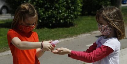 Dos niñas con mascarillas se limpian las manos con solución hidroalcohólica.