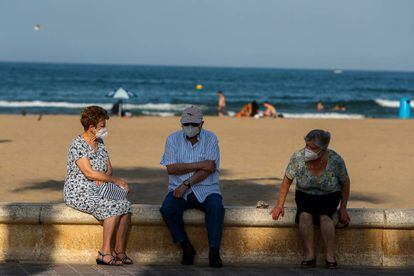 Tres personas mayores descansan en el paseo marítimo de la playa de la Malvarrosa (Valencia).