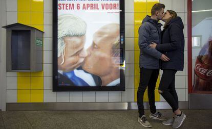 Una pareja se besa junto a un poster con una caricatura en la que el pol&iacute;tico holand&eacute;s Geert Wilders besa al presidente ruso Vald&iacute;mir Putin en el metro de &Aacute;msterdam.