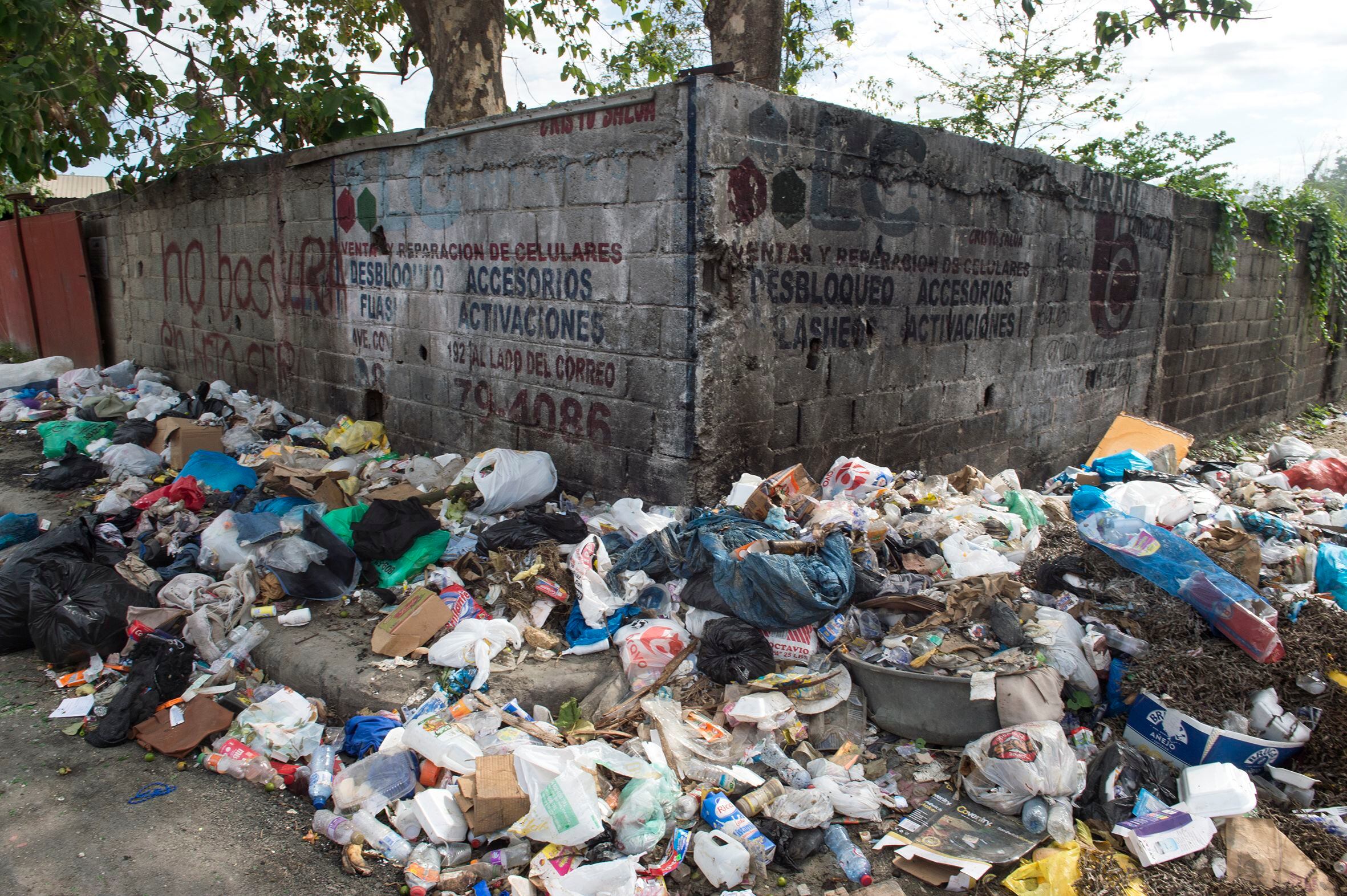 Trash on a sidewalk in San Cristóbal next to a sign on the wall that reads 'No trash dumping.'