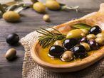 wooden bowl in the foreground with rosemary olives and virgin oil on the wooden table