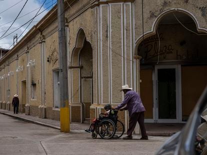 Un hombre empuja la silla de ruedas de su mujer frente a un hotel quemado por el narcotráfico en Aguililla, Estado de Michoacán, el 8 de julio de 2021.