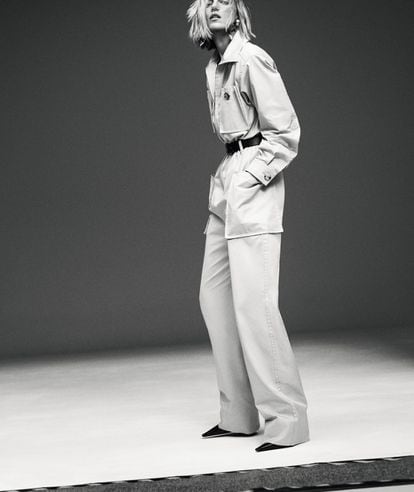 Anja Rubik wears a long-sleeved jumpsuit, earrings, belt and shoes, all by SAINT LAURENT BY ANTHONY VACCARELLO.